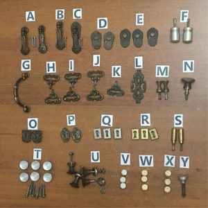 以下が含まれることがあります： 引き出しの取っ手、ノブ、蝶番、鍵穴カバーなど、アンティーク調のキャビネット金具の詰め合わせ。金具は金属製で、真鍮、ブロンズ、ニッケルなど、さまざまな仕上げが施されています。