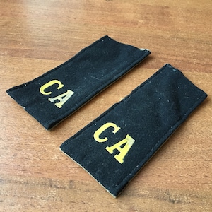 以下が含まれることがあります： 黄色の糸で「CA」と刺繍された黒い布のパッチが2つ