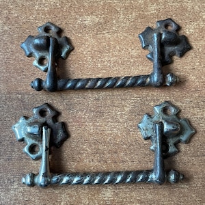 May include: Two antique drawer pulls with a twisted metal design. The pulls are made of metal and have a dark finish. The pulls are attached to a decorative metal plate with a scalloped edge.