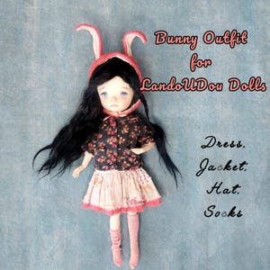 May include: A doll with long black hair wearing a pink bunny ear hat, a dark floral print jacket with pink buttons, a light-colored patterned skirt, and pink socks. Text on the image reads: Bunny Outfit for LandoUDou Dolls. Dress. Jacket. Hat. Socks.