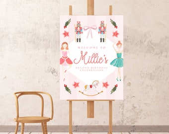 May include: Pink welcome sign with a white border and a white circle in the center. The text "Welcome to Millie's Second Birthday Celebration" is inside the circle. The sign is decorated with a nutcracker, a ballerina, a rocking horse, and holly.