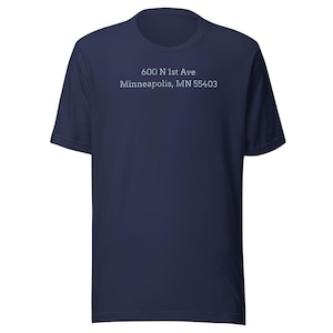 Puede incluir: Camiseta azul marino con el texto blanco "600 N 1st Ave Minneapolis, MN 55403". La camiseta tiene mangas cortas y cuello redondo.