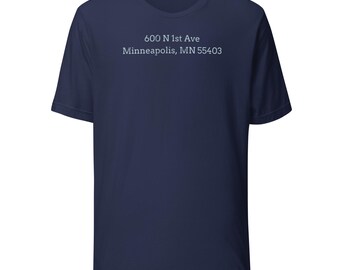 May include: Navy blue t-shirt with the text "600 N 1st Ave Minneapolis, MN 55403" printed in white. The shirt has short sleeves and a crew neck.