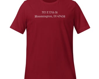 May include: A maroon short-sleeve t-shirt with the text "701 E 17th St Bloomington, IN 47408" printed in white. The shirt is made of a soft material and has a classic crew neck design. This casual tee is suitable for everyday wear.