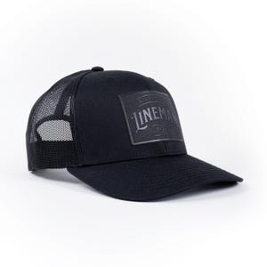 May include: Black trucker hat with a black mesh back and a black square patch with the text "TRUE NORTH" and "LINEMAN" in a vintage font.