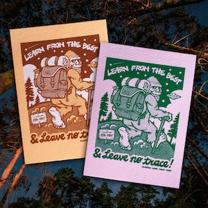May include: Two illustrated postcards with a green and brown color scheme. The postcards feature a cartoon Bigfoot character wearing a backpack and hiking with a stick. The text on the postcards reads "Learn from the best & Leave no trace!"