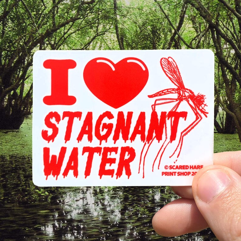 May include: A white sticker with the words "I ❤️ STAGNANT WATER" in red, along with a red heart and a mosquito illustration. The sticker is held in front of a swampy background.