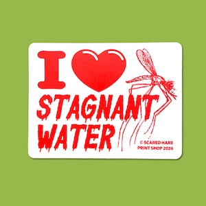 May include: A white sticker with a red graphic that reads "I ❤️ STAGNANT WATER." A red heart and a mosquito are also featured. The sticker has rounded corners and the text "SCARED HARE PRINT SHOP 2024."
