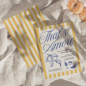May include: Two bridal shower invitations with yellow and white striped borders. The main invitation reads "That's Amore" in elegant blue script, with event details and lemon illustrations. A few mandarin orange slices are in the background.