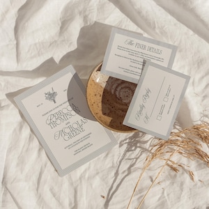 May include: Wedding stationery set with a floral design and striped borders. The set includes an invitation, details card, and RSVP card. The invitation text reads "Rebecca Thompson and Nicholas Greene". The cards are arranged on a ceramic plate.