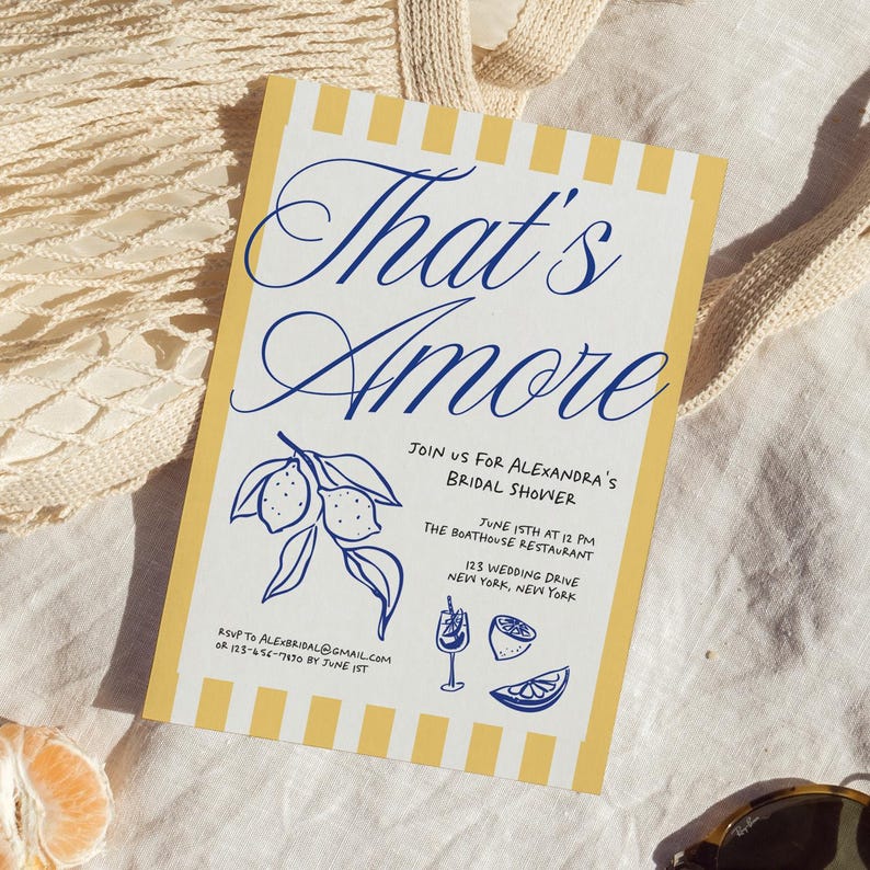 May include: A bridal shower invitation with a yellow and white striped border. The invitation features the words "That's Amore" in elegant blue script. Additional text includes details for the event, along with lemon illustrations.