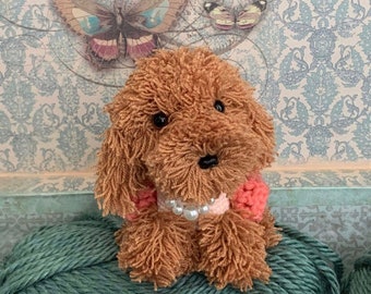 May include: Crocheted brown poodle toy wearing a pink sweater and a pearl necklace. The toy is sitting on a green yarn ball. Crochet pattern only.
