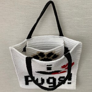 May include: White crocheted tote bag with black handles and a paw print design. The bag has the word "Pugs!" written on the front in black.