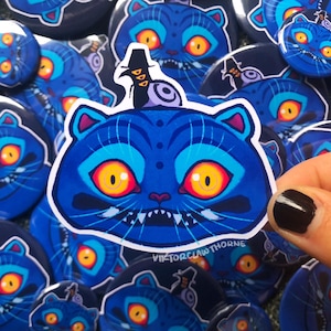 Könnte beinhalten: Eine Ansammlung blauer Aufkleber und Buttons mit Katzenmotiven, orangefarbenen Augen und aufwendigen Designs. Ein Aufkleber wird von einer Hand mit einem schwarz lackierten Nagel gehalten. Der Text "VIKTORCLAW THORNE" ist sichtbar.