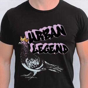 May include: Black t-shirt featuring a graphic of a pigeon wearing a gold crown. The text "URBAN LEGEND" is above the pigeon in a bubble letter style with a pink outline. The pigeon has a white and black pattern.