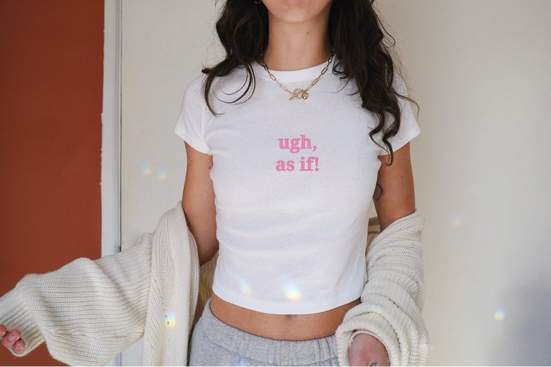 Puede incluir: Camiseta blanca recortada con texto rosa que dice "ugh, as if!"