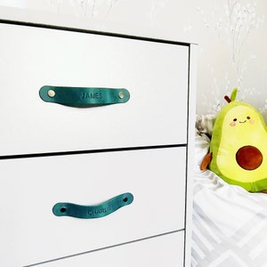 May include: White dresser with two drawers featuring green leather pulls with the names "JAMES" and "CHARLIE" engraved on them.