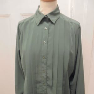 May include: A long-sleeved, green button-down shirt with a pleated front and a collared neckline.