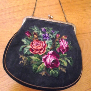 Könnte beinhalten: Eine schwarze Samt-Handtasche mit einem silbernen Kettenriemen und einem floralen Stickmuster mit rosa, roten und violetten Rosen.