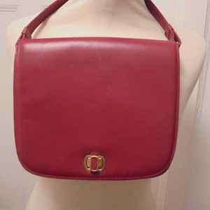 Può includere: Una borsa a tracolla in pelle rossa con una chiusura dorata.