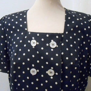 Peut inclure: Une robe à pois noirs et blancs avec un col carré et des manches courtes. La robe a une fermeture à double boutonnage avec quatre boutons.