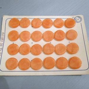 May include: A sheet of orange plastic buttons, arranged in rows on a white card. The card has the text "Art 1663 36. Fb. 23" printed on it.