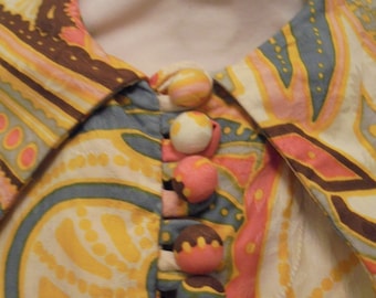 May include: A yellow, blue, pink and brown patterned blouse with a collar and a row of decorative buttons down the front.