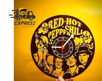 May include: A black and yellow clock featuring the words "Red Hot Chili Peppers" and band member portraits. The clock has a black face with white hands and Roman numerals. The clock is held against a yellow background.