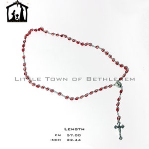 May include: Red glass bead rosary with a silver cross and a silver charm. The rosary is 22.44 inches long.