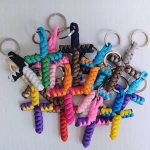 May include: A collection of colorful, braided, cross-shaped keychains with silver key rings. The keychains are made of different colored cords and are tied together in a knot.