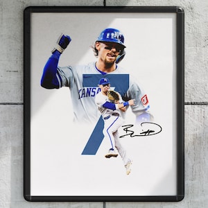 May include: Framed print featuring a baseball player in a blue helmet and jersey, with the word "KANSAS" visible. The image includes a signature and a blue number 7 overlay. The background is a light gray.