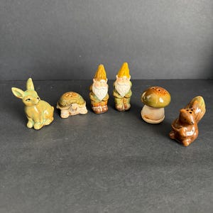 May include: A collection of ceramic figurines, including a green rabbit, a turtle, two gnomes, a mushroom, and a squirrel. The figurines are painted in various colors, with details like the gnomes' hats and the squirrel's bushy tail.