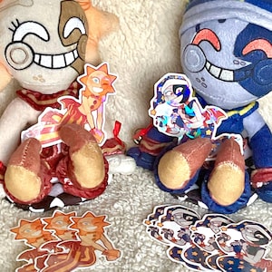 May include: Two plush toys, one sun-themed and one moon-themed, with smiling faces and detailed features. Accompanying the toys are several stickers featuring the same characters in various poses. The toys and stickers are set against a soft, textured background.