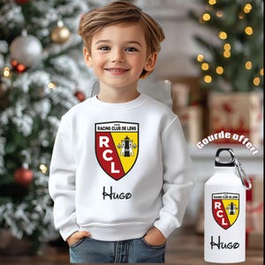 Peut inclure: Un sweat-shirt blanc avec le logo du Racing Club de Lens, le nom "Hugo", et une gourde assortie. Le logo est un écusson aux couleurs rouge, jaune et noir. La gourde a un mousqueton argenté.
