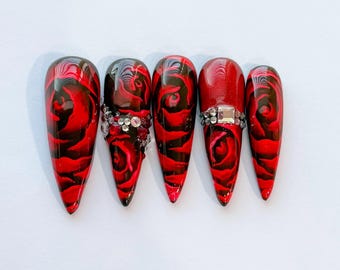 May include: Set of six long, stiletto-shaped false nails with a black and red rose design. Each nail has a clear rhinestone accent.