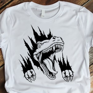 May include: A white t-shirt with a black graphic of a dinosaur head breaking through the fabric. The dinosaur has sharp teeth and claws.
