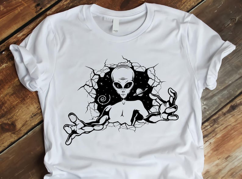 May include: White t-shirt with a black and white graphic print of an alien reaching out from a cracked wall.