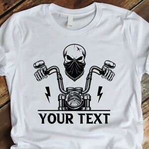 May include: White t-shirt with a black and white graphic of a skull wearing a bandana and riding a motorcycle. The text "YOUR TEXT" is printed below the graphic.