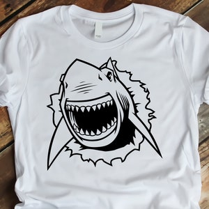 May include: A white t-shirt with a black and white graphic of a shark's head breaking through a wall.