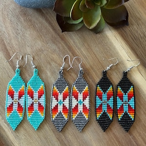 May include: Three pairs of beaded dangle earrings in a leaf shape. The first pair is turquoise, the second is dark grey, and the third is black. Each earring features a geometric pattern in red, orange, white, and light blue beads with silver hooks.