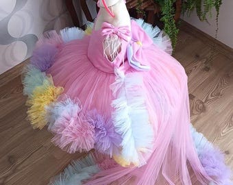 May include: A pink tulle dress with a rainbow-colored tulle trim and a unicorn headband. The dress has a long train and is perfect for a special occasion.