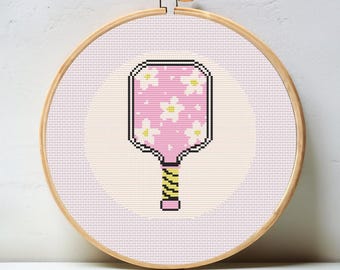 May include: A pink and white paddle with a yellow and black handle. The paddle has a floral pattern with white flowers on a pink background. The paddle is in a wooden embroidery hoop.