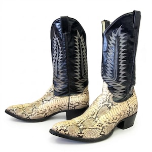 Pode incluir: Um par de botas de cowboy com um padrão de pele de cobra no pé e uma parte superior de couro preto. As partes superiores de couro preto são decoradas com costuras prateadas. As botas têm uma biqueira pontiaguda e um salto empilhado.