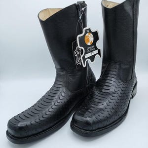 May include: A pair of black leather cowboy boots with a square toe. The boots feature a textured pattern on the vamp and a tall shaft. One boot has a tag that reads "GENUINE LEATHER".