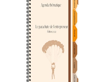 May include: A tan and brown spiral bound notebook with the title "Le parachute de l'entrepreneur" and the text "Edition 2022". The cover features a silhouette of a person skydiving with a parachute.