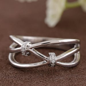May include: A silver-colored ring with a unique, intertwined design. The ring features two small, diamond-studded accents. The band has a polished finish, creating a modern and elegant look. The ring is a piece of jewelry.