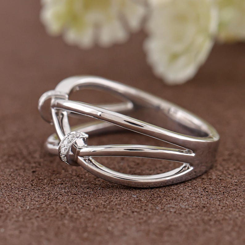 May include: A silver ring with a unique design. The ring features a series of intertwined bands, creating an open, airy look. Small, clear stones are set at the intersection of the bands, adding a touch of sparkle. The ring is set against a brown background.