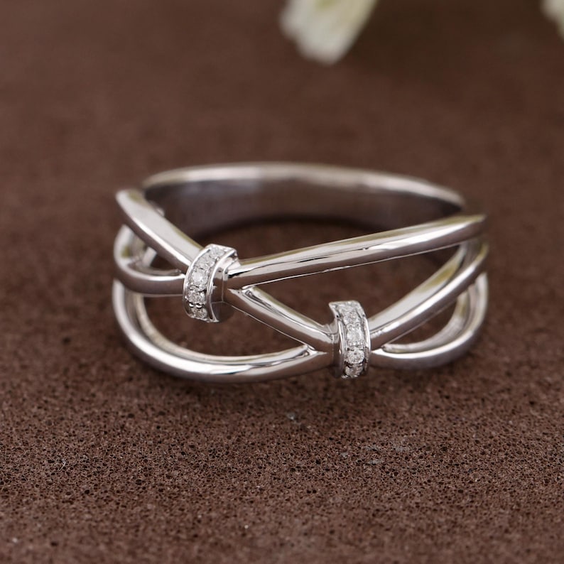 May include: A silver ring with a unique design. The ring features a series of intertwined bands, with two sections adorned with small, sparkling stones. The ring is set against a brown background.