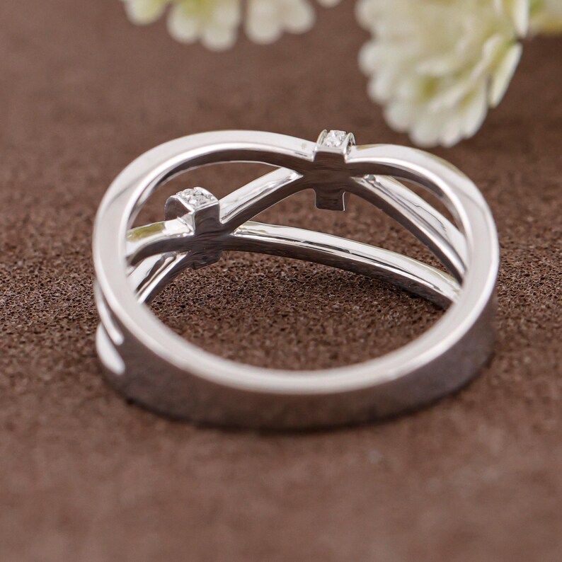 May include: A silver ring with a unique design, featuring two small square-shaped gemstones. The ring has an intertwined, openwork design. The ring is set against a brown background, with a blurred white flower in the background.