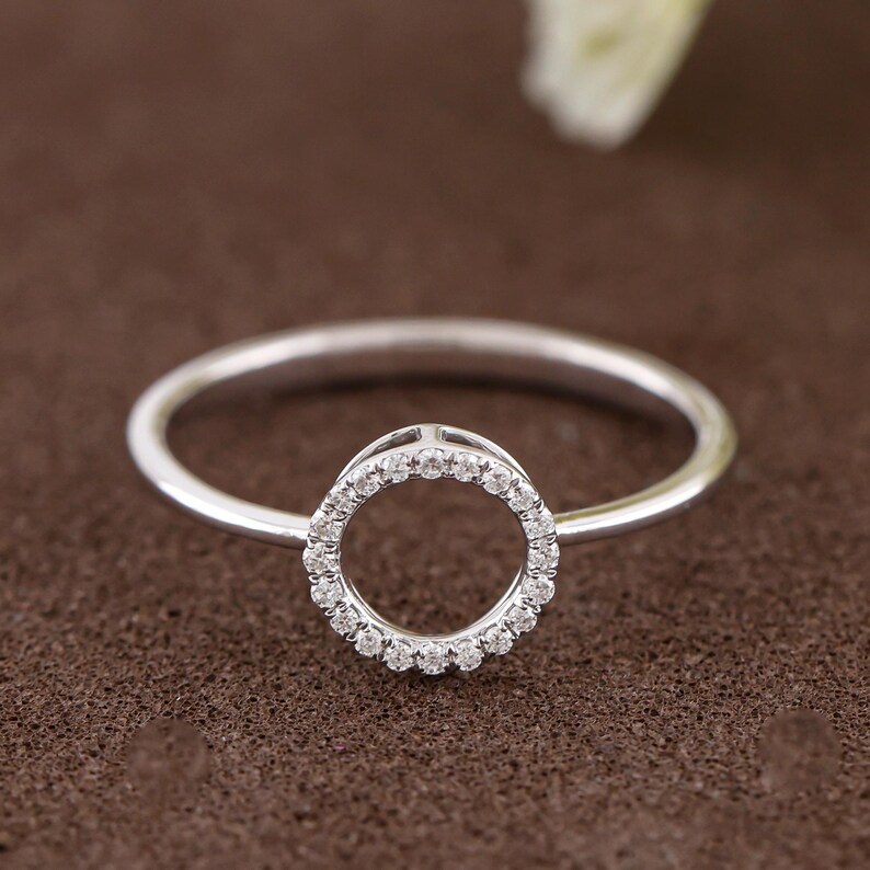 Puede incluir: Un anillo de plata con un dise&ntilde;o circular. El c&iacute;rculo est&aacute; incrustado con peque&ntilde;as piedras preciosas transparentes. La banda del anillo es delgada y pulida, sobre un fondo marr&oacute;n.